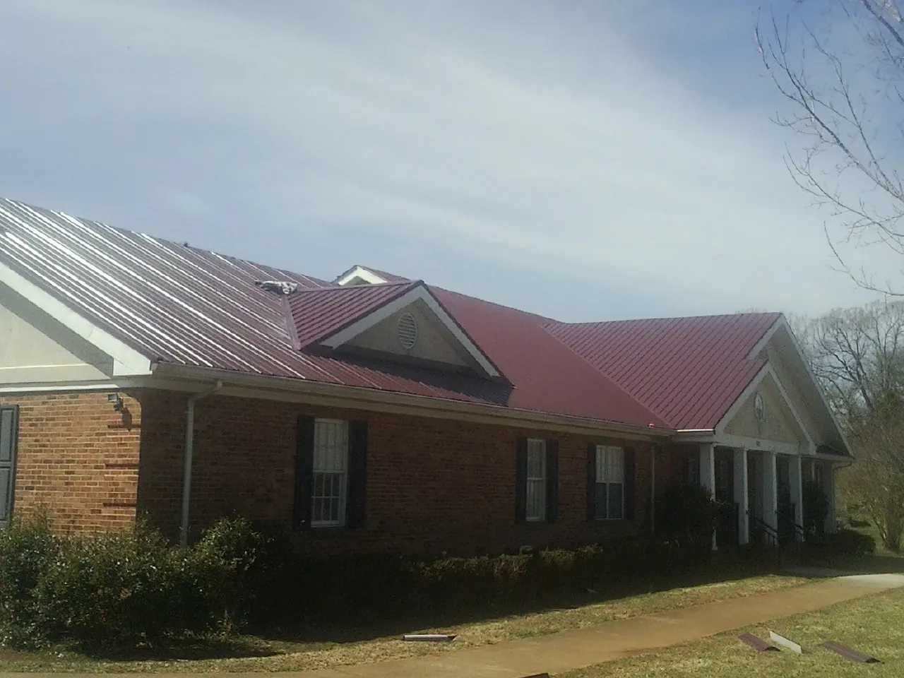 Red metal roof with gabled entries on a long brick building, from a Hail Damage Roof Repair job in Franktown
