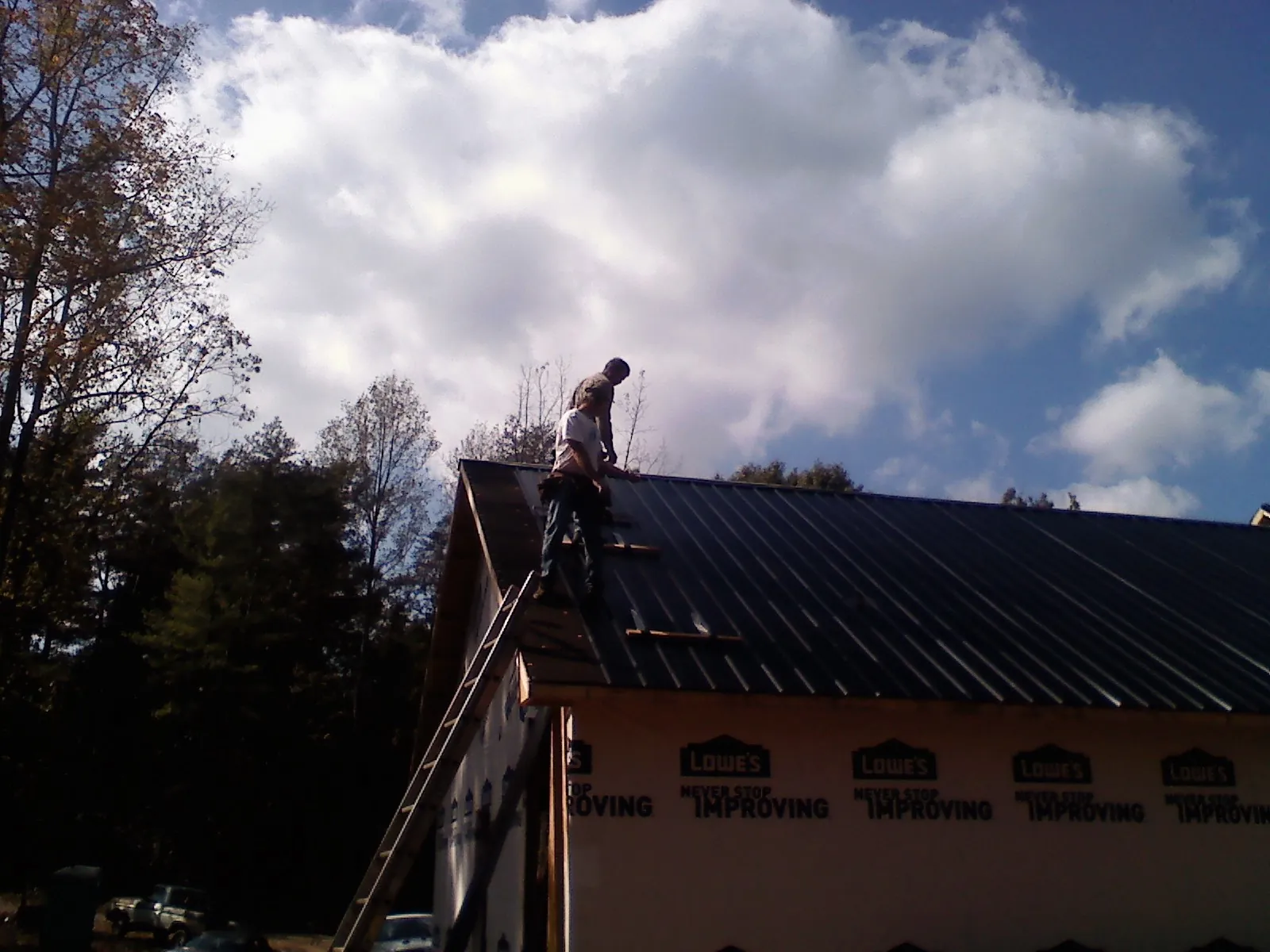 Roofer fastening dark metal panels high against a cloudy sky, from a Roof Inspection job in Franktown